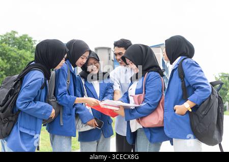 A group of Muslim students gathers outdoors, enthusiastically reviewing schoolwork. The young women are dressed in hijabs and backpacks, symbolizing a Stock Photo