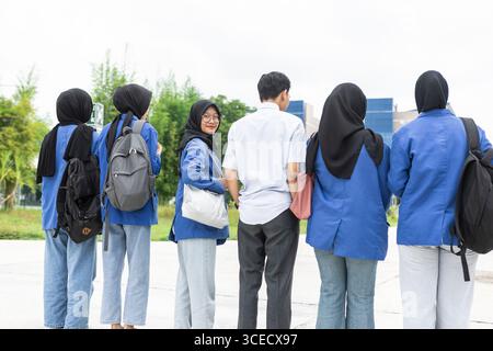 A group of Asian Muslim students are walking towards their school, ready to start a new semester. They are wearing casual outfits and carrying backpac Stock Photo