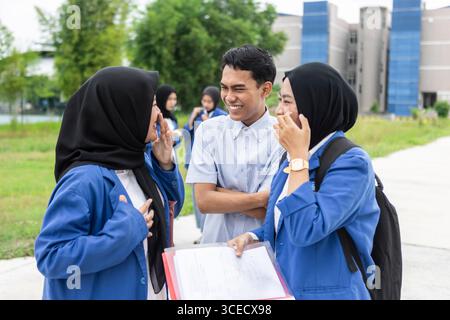 Asian Muslim students enjoy a lighthearted moment on their return to school, highlighting friendship and cultural diversity on a vibrant university ca Stock Photo