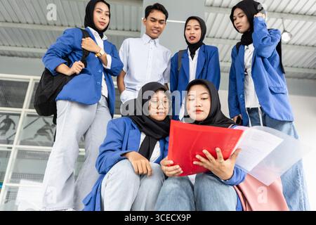 A group of Asian Muslim students gather to review school papers. They wear uniforms and appear focused, demonstrating their dedication to learning Stock Photo