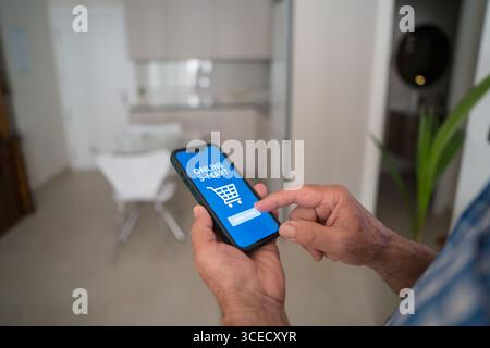 Cropped unrecognizable senior man using a smartphone to shop online from home. The app interface displays an online cart, emphasizing the convenience Stock Photo