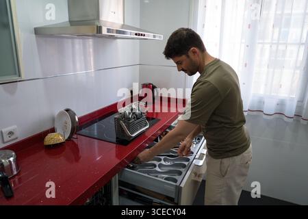 A man is organizing utensils in a modern kitchen. He carefully arranges cutlery in a drawer, demonstrating efficient household management and attentio Stock Photo
