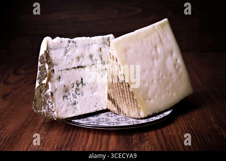 A close-up of a cheese wedges placed on an elegant white plate with dark patterns, set against a rustic wooden background. The cheese displays a rich Stock Photo