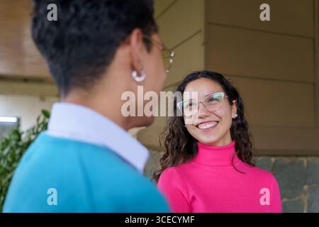 A Gen Z man and woman are engaged in a friendly conversation. The young man, with short hair, is smiling at the woman in glasses who is joyfully respo Stock Photo