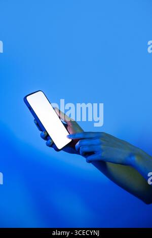 A hand interacts with a modern smartphone, glowing under vibrant neon lights. The colorful ambiance highlights technology and connectivity in a digita Stock Photo