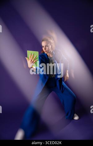 A young woman in a blue suit interacts with a glowing green device, emphasized by beams of light, representing an innovative technological concept in Stock Photo