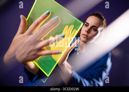 A young woman interacts with a futuristic device, exploring augmented reality. Her hands hover over a vibrant, glowing interface, symbolizing innovati Stock Photo
