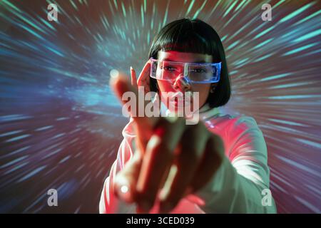 Latin woman interacts with an immersive virtual reality environment, wearing VR glasses. The scene is vibrant with colorful lights, symbolizing futuri Stock Photo
