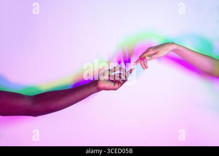 Two multiethnic hands reaching towards each other against a vibrant background with dynamic, colorful light. The image embodies unity, diversity, and Stock Photo