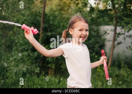 A joyful girl playing with soap bubbles in a lush garden, embodying the carefree essence of childhood during a bright summer day. Perfect representati Stock Photo