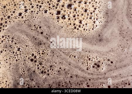 A close-up macro image showcasing the rich, textured surface of coffee foam. Swirls and bubbles create an intricate pattern across the creamy beige ba Stock Photo