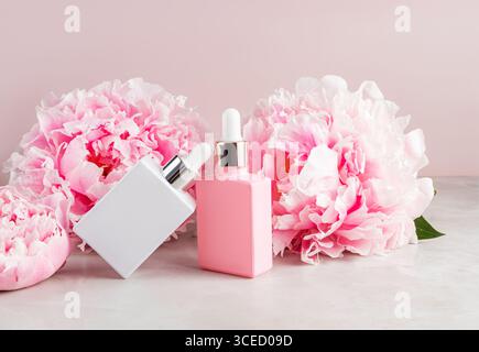 Two stylish cosmetic bottles, one white and one pink, are artfully positioned among lush pink peonies on a soft, neutral background, creating a luxuri Stock Photo