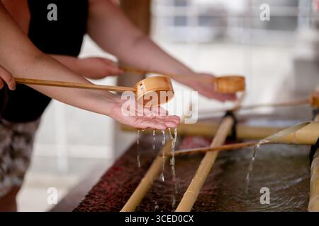 Close-up of people performing the traditional hand washing ritual at Shitennō-ji temple in Osaka, Japan, using wooden ladles to purify hands in clear Stock Photo