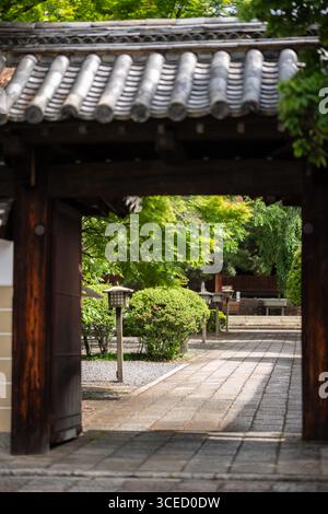 A serene view through the traditional wooden gate at Daihōonji Temple, Kyoto, revealing a tranquil garden path lined with greenery and classic Japanes Stock Photo
