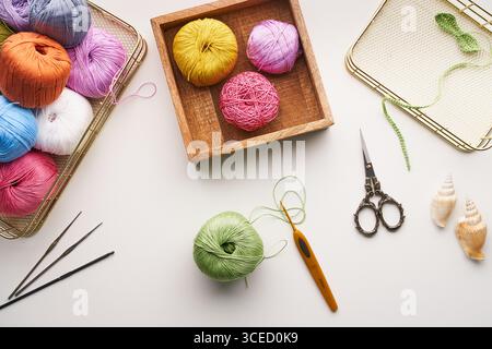 Top view of various colored yarns, crochet hooks, and ornate scissors arranged for needlework and jewelry creation. Perfect for showcasing handcrafted Stock Photo