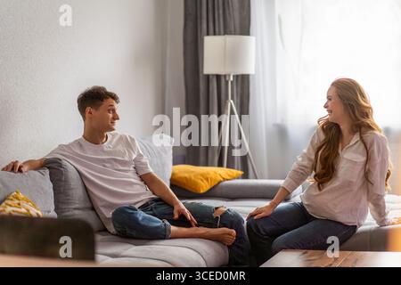 Young couple expecting a baby relaxing on a cozy couch. The man and woman are smiling, enjoying a peaceful moment together in their home as they prepa Stock Photo