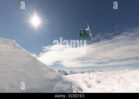 A snowboarder executes an impressive trick in midair, soaring above pristine snow-covered mountains under a vibrant blue sky, capturing the essence of Stock Photo