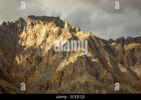 Stunning view of a rugged mountain range in Spiti Valley, India, under dramatic cloudy skies. The sunlight casts shadows, highlighting the rugged terr Stock Photo