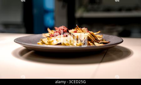 A gourmet dish featuring artichokes elegantly arranged with vibrant, finely chopped toppings on a sleek black plate. Perfect for showcasing culinary a Stock Photo