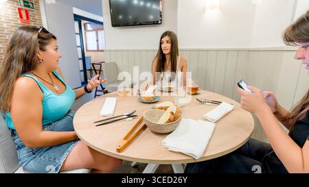 Three friends gather around a wooden table in a cozy restaurant, engaging in conversation and enjoying their meal. The atmosphere is relaxed and invit Stock Photo