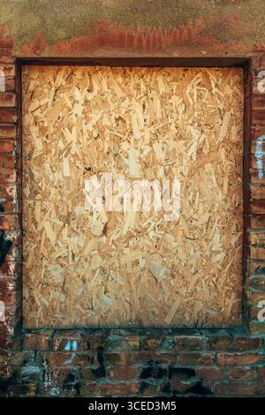 Close-up of a weathered wooden panel covering a window on an old red brick wall, ideal for background or texture use, vertical image Stock Photo