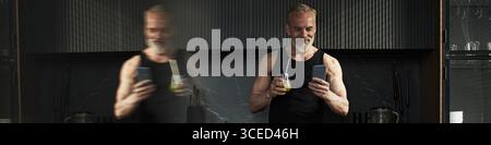 Middle Aged Caucasian Man Smiling While Using Smartphone and Drinking Juice Stock Photo