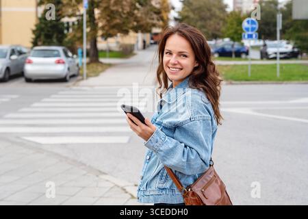 Cheerful female holding smartphone on city street Stock Photo
