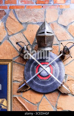 A knight's helmet and sword are mounted on a wall. The helmet is decorated with a cross and the sword is decorated with a red and white design. Scene Stock Photo