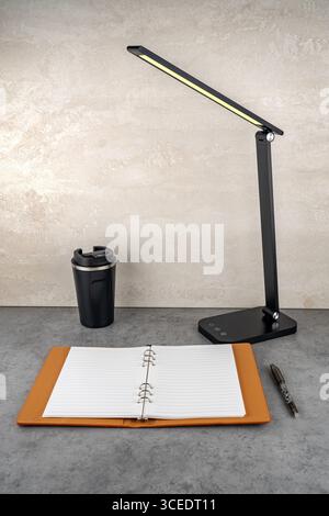 A modern table lamp with soft light illuminates an open notebook on the desk. Stock Photo