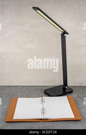 A minimalist LED lamp with soft light illuminates a notebook at the workplace. Stock Photo