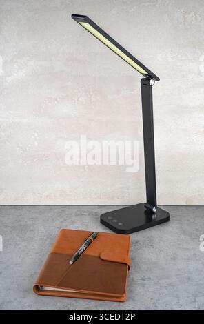 A modern design table lamp emits soft light onto the table and notebook. Stock Photo