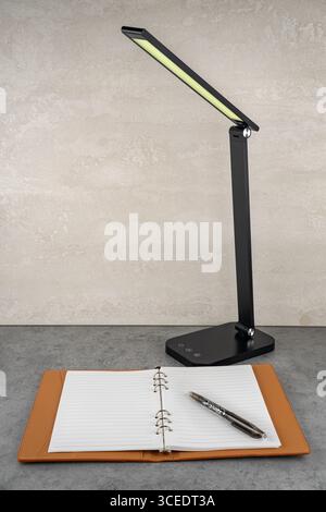 A modern designer lamp with soft light harmoniously illuminates the notebook on the table. Stock Photo