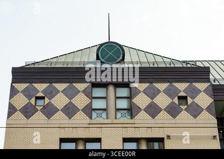 Geometric patterns decorate the upper facade of a beige brick building with a green circular vent above. Stock Photo