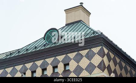 A patterned facade with diamond-shaped tiles supports a green metal roof topped with a circular vent and brick chimney. Stock Photo