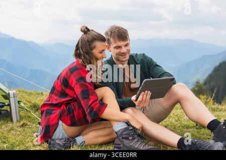 Modern digital nomad couple camping in nature, using a tablet to stay connected and entertained while relaxing and enjoying the great outdoors Stock Photo