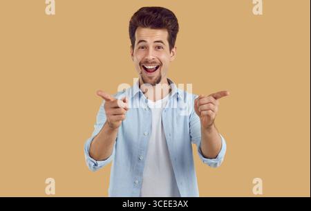 Smiling laughing happy bearded man pointing index fingers to camera on beige background. Stock Photo