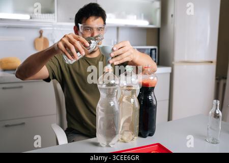 Home gardening enthusiast wearing safety glasses carefully pouring liquid from glass bottle through funnel into plastic bottle, creating plant Stock Photo