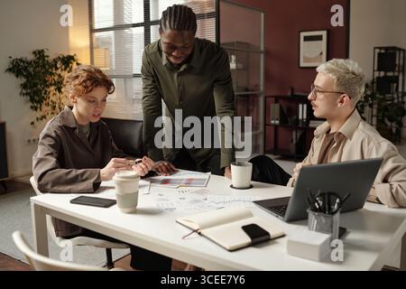 Group of three diverse young male and female employees discussing business strategy at work in modern office Stock Photo