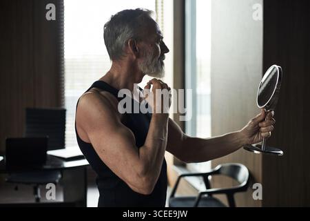 Middle Aged Caucasian Man Grooming Beard While Looking into Handheld Mirror Stock Photo