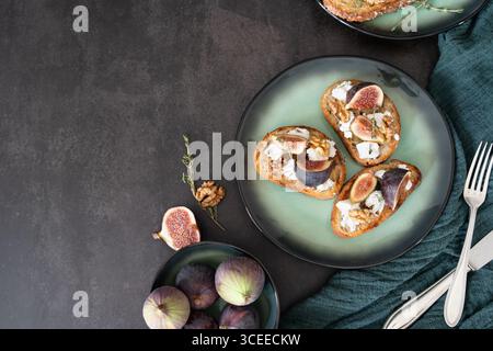 Horizontal top view of three rustic fig and goat cheese toasts with thyme and walnuts on green plate and towel Stock Photo
