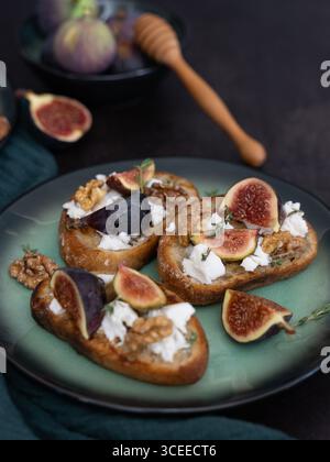 Front view vertical close up of three fig and goat cheese toasts on green plate with honey dipper, walnuts, thyme, green kitchen towel, savory sweet m Stock Photo