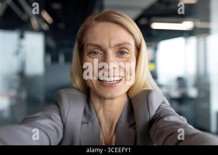 Confident professional woman smiling and taking a selfie in a modern office environment. Capturing an empowering moment reflecting positivity and professionalism. Stock Photo