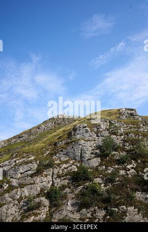 Cliff and hill with blue sky and clouds in countryside with small group of people on top Stock Photo