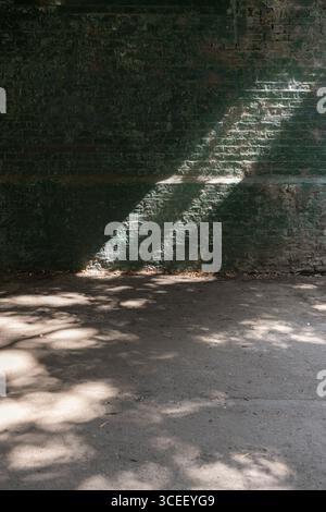 a strong beam of sunlight diagonally traversing the upper part of a structure, railway bridge, and casting distinct shadows on both the wall and the g Stock Photo