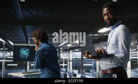 Smiling data center engineering team on industrial platform collaborating on neural network software tasks. Jolly server hub colleagues working together, visualizing large language model architecture Stock Photo
