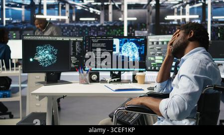 Man in wheelchair dissatisfied with server farm AI analytics metrics. Data center admin with paraplegia frustrated by glitches while automating tasks using node tree programming tool, camera A Stock Photo