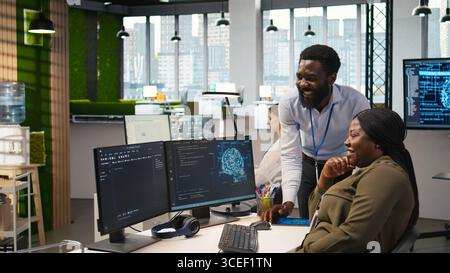 Cheerful programmers in office enjoying conversation while automating repetitive tasks with AI. Happy coworkers chatting, using artificial intelligence to speed up feature implementation, camera A Stock Photo