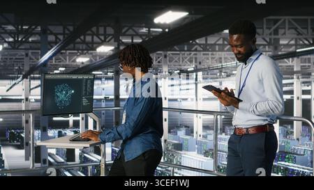 Engineers working together on data center industrial platform, completing software updates. Server hub colleagues doing brainstorming, finetuning server rig configurations Stock Photo