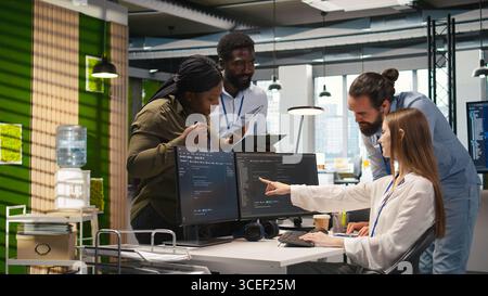 Welcoming team assisting intern developing artificial intelligence models for business analytics. Friendly coworkers helping junior dev running simulations for AI driven forecasting, camera A Stock Photo