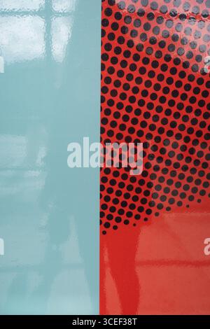 abstract design concept with partial wall of blue shiny paint and other part of wall of red plastic with black holes reflection of person with camera Stock Photo